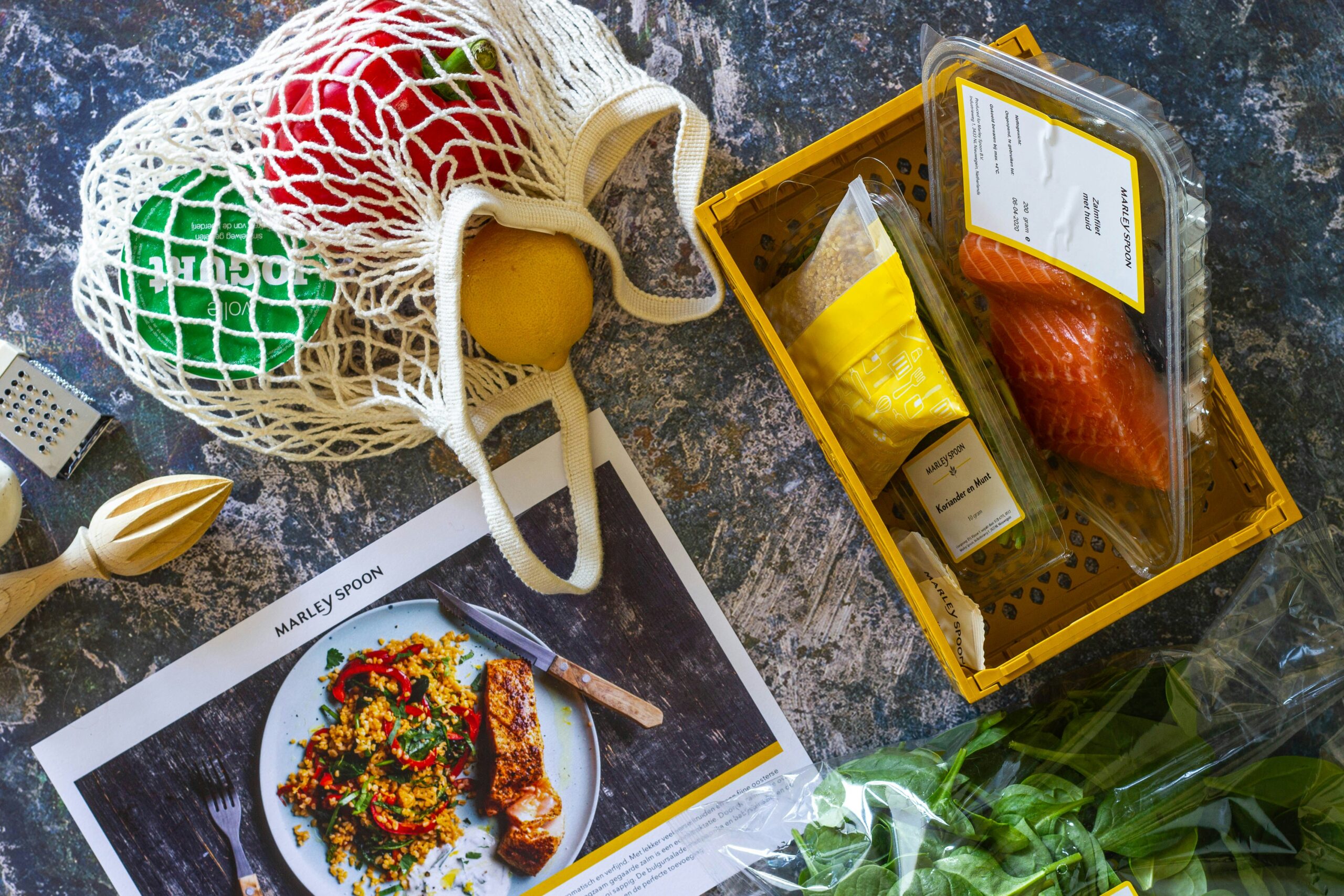 Grocery delivery meal kit with fresh vegetables, salmon, packaged ingredients, and a recipe card arranged on a kitchen countertop.